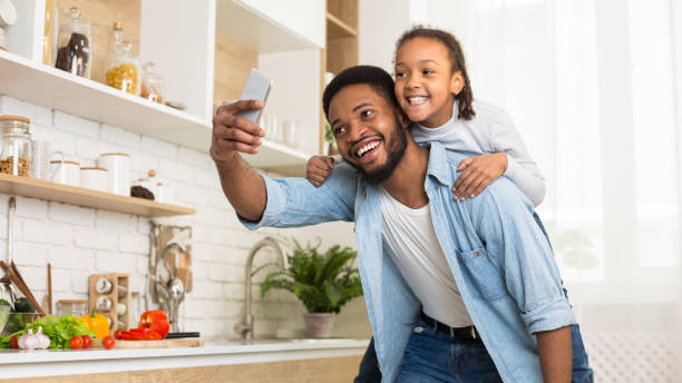 istock Afro dad and daughter taking selfie on cellphone in kitchen 1165676214