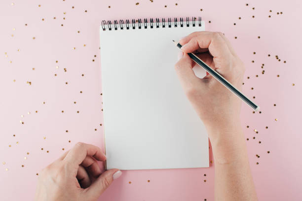 istock Woman's hand writing in empty notebook decorated with Christmas decorations on the blue background. Mock up concept. Top view, flat lay, copy space 1165677430