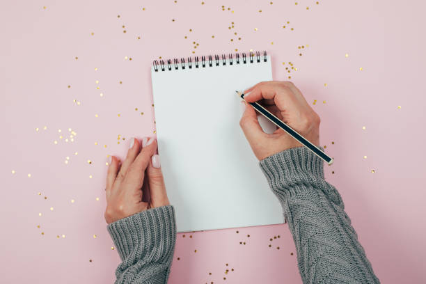 istock Woman's hand writing in empty notebook decorated with Christmas decorations on the blue background. Mock up concept. Top view, flat lay, copy space 1165677452