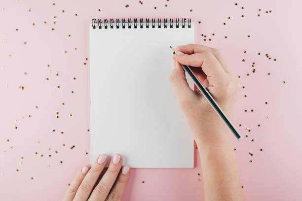 istock Woman's hand writing in empty notebook decorated with Christmas decorations on the blue background. Mock up concept. Top view, flat lay, copy space 1165677477