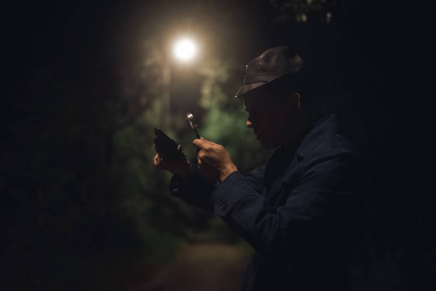 Detective. Detective agent with a gun in his hand is watching through a magnifying glass and searching for a clue. man holding gun at night in the city stock pictures, royalty-free photos & images