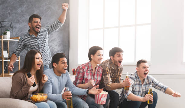 Friends cheering favourite football team, watching match at home Emotional friends cheering favorite football team, watching match at home. Copy space excited football fan cheering for his team on tv stock pictures, royalty-free photos & images