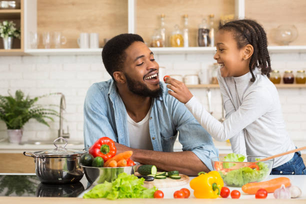 istock Lovely afro girl feeding her dad while cooking 1165679294