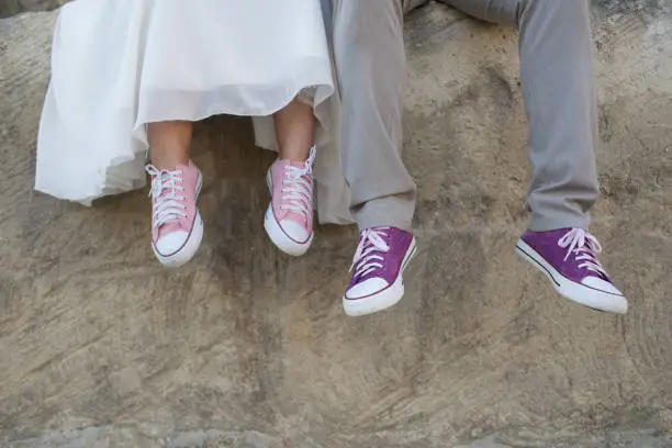 The bride and groom are sitting with their legs dangling in purple sneakers.- Image