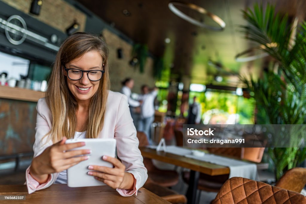 Pretty young female manager using modern digital tablet at cafe Young businesswoman drinking coffee and using tablet computer in cafe. Happy young businesswoman using tablet computer in a cafe. Young female entrepreneur reading electronic book on digital tablet Women Stock Photo