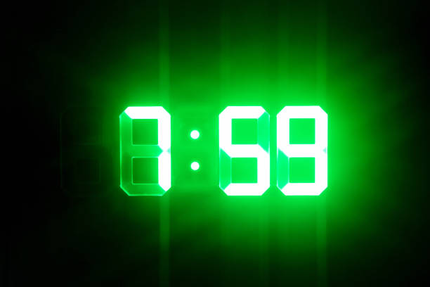 istock Green glowing digital clocks in the dark show 7:59 time 1165684746