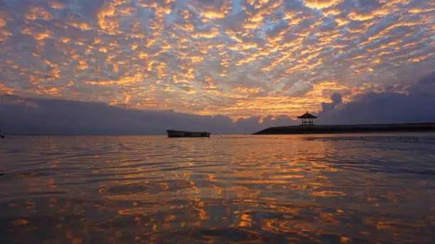 Golden and colorful sunrise sky. Golden sunrise clouds color reflections on water. Morning scenery. Sanur beach nature beach landscape view and the glow background. Bali, Indonesia.