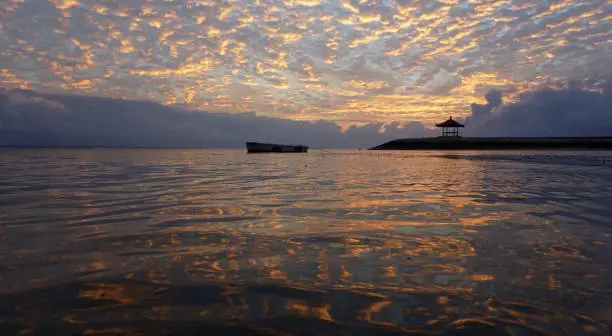 Golden and colorful sunrise sky. Golden sunrise clouds color reflections on water. Morning scenery. Sanur beach nature beach landscape view and the glow background. Bali, Indonesia.