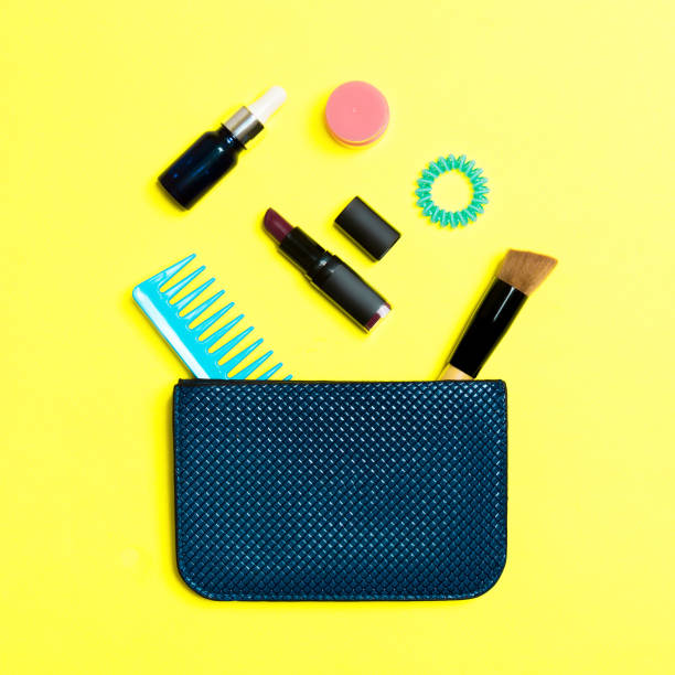 make up products spilling out of cosmetics bag on yellow background with empty space for your design - pampering nail polish make up spilling imagens e fotografias de stock