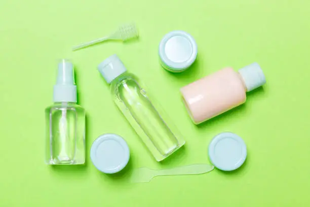 Set of travel size cosmetic bottles on green background. Flat lay of cream jars. Top view of bodycare style concept.