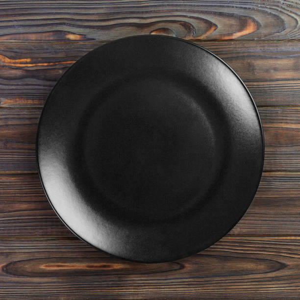 istock Round plate on table. black dish on wooden background. copy space 1165687371