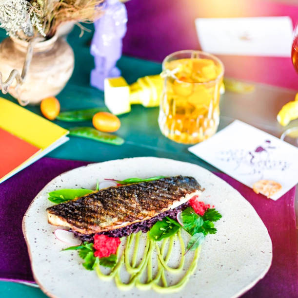 roasted dorado or sea bream fish with lemon and orange slices, spices, fresh parsley and spinach on white platter on old wooden table with ingredients on background, horizontal view from above