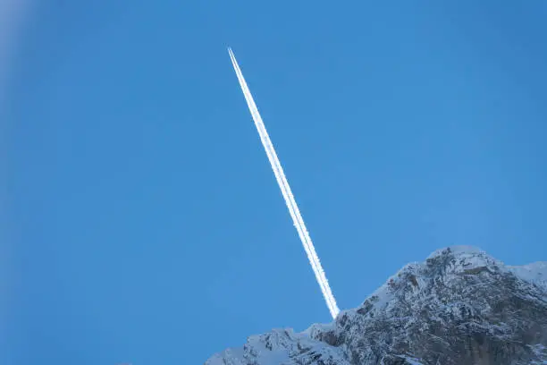 An aircraft with its contrail raising behind a big rocky mountain