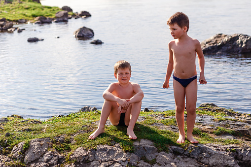 two boys in bathing shorts playing on the river in the summer