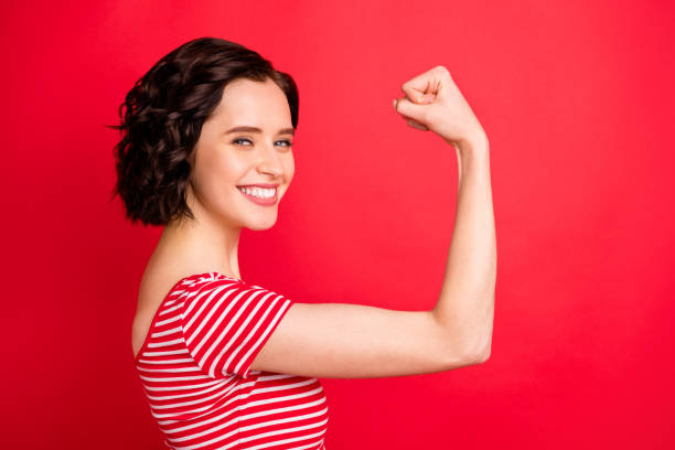 Photo of rejoicing wavy curly woman after having done two pushups while isolated with red background Photo of rejoicing wavy, curly woman after having done two pushups while isolated with red background bicep photos stock pictures, royalty-free photos & images