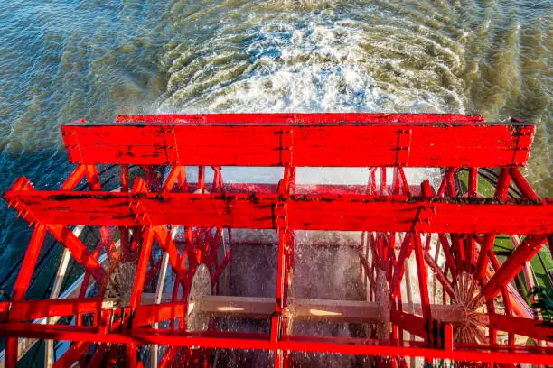 The red wooden paddle-wheel of an old steamboat. On the move while cruising, with the paddles chopping into the water.