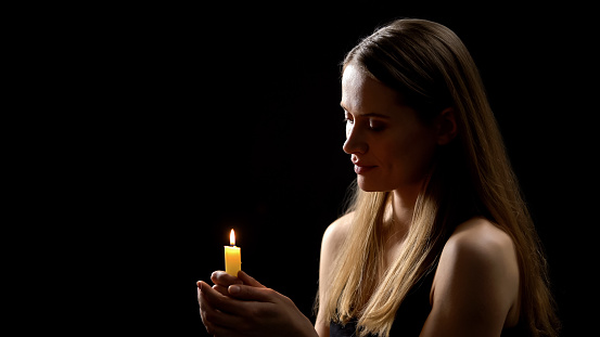 Young woman holding candle in hands, remembrance day, praying for dead relatives