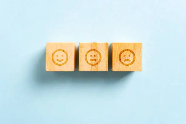 Photo of Happy, neutral/serious and frown face emojis on wood blocks toys and blue background. Rating concept.