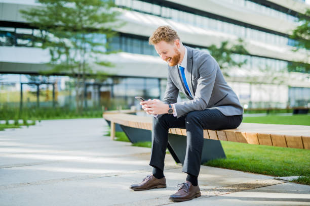 istock Happy young businessman sitting outdoors and using phone. 1165712011