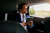 Handsome businessman sitting with digital tablet on the backseat of the car stock photo