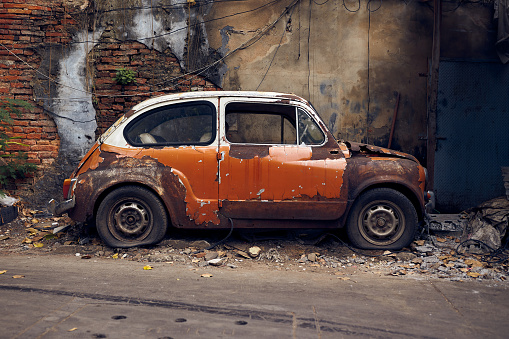Old abandoned rusty white/orange vintage car wreck in an old street