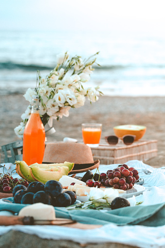 Seaside beach picnic on sand concept,  cheese platter with fruits - dark red grapes and melon and plums, crackers and nuts, copy space, relaxed resort eating, beautiful lifestyle concept