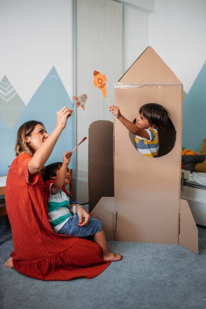 очаровательные маленькие мальчики и их мать, играющая с картонной ракетой дома - science education school offspring стоковые фото и изображения