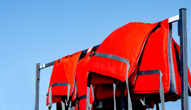 stos czerwonych kamizelek ratunkowych używanych przez ratowników siedzących na grabie w pobliżu plaży w sezonie letnim przed błękitnym niebem . - life jacket buoy sign sky zdjęcia i obrazy z banku zdjęć