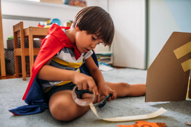 自宅で段ボールロケットで遊ぶスーパーヒーローのような服を着たかわいい男の子 - superhero child creativity little boys ストックフォトと画像