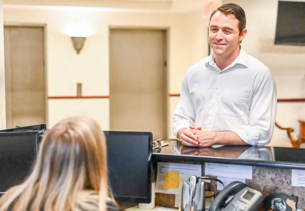 istock Man stands at at reception desk and talks to a receptionist in an office setting 1165721869