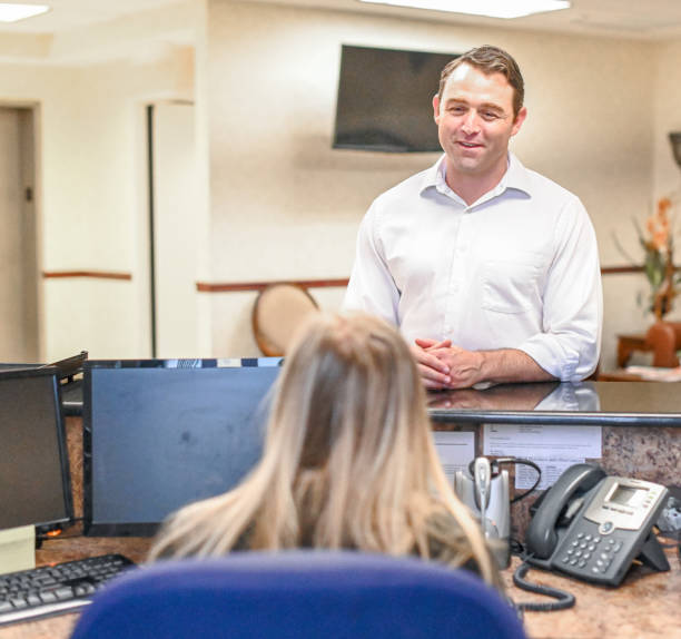 istock Man stands at at reception desk and talks to a receptionist in an office setting 1165721874