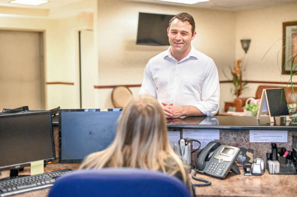 istock Man stands at at reception desk and talks to a receptionist in an office setting 1165721875