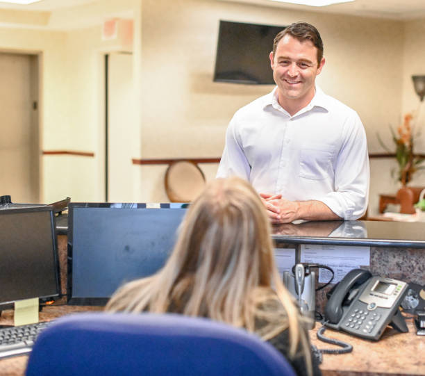 istock Man stands at at reception desk and talks to a receptionist in an office setting 1165721912