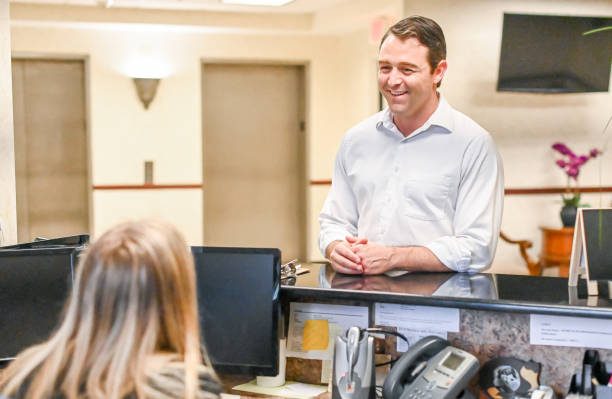 istock Man stands at at reception desk and talks to a receptionist in an office setting 1165722061