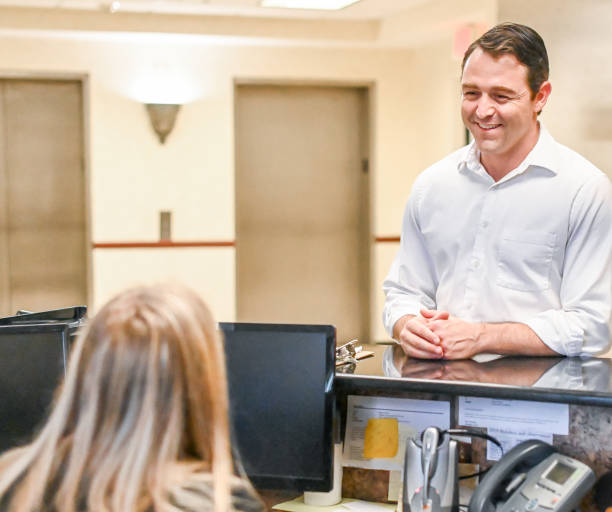 istock Man stands at at reception desk and talks to a receptionist in an office setting 1165722067