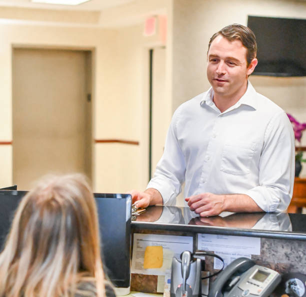 istock Man stands at at reception desk and talks to a receptionist in an office setting 1165722108