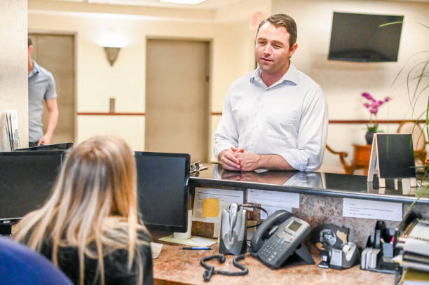 istock Man stands at at reception desk and talks to a receptionist in an office setting 1165722111