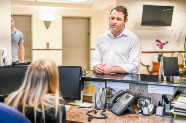 istock Man stands at at reception desk and talks to a receptionist in an office setting 1165722153
