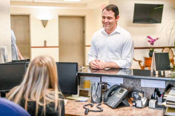 istock Man stands at at reception desk and talks to a receptionist in an office setting 1165722163