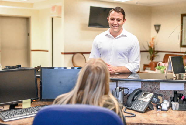 Man stands at at reception desk and talks to a receptionist in an office setting