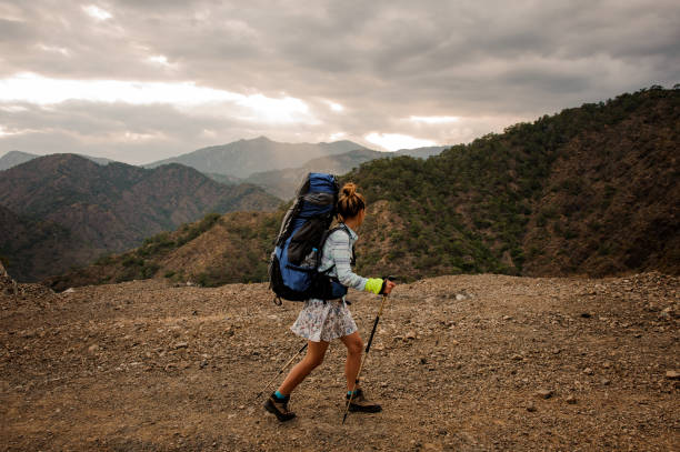 istock Side view girl with backpack and hiking sticks walking on the dirt road 1165728507