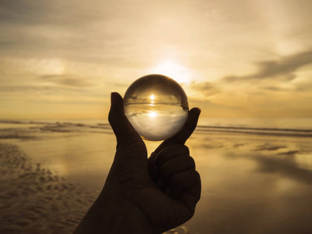 istock hand holding crystal ball with golden sunrise reflection at summer beach. 1165732839