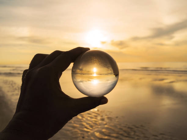 boule de cristal de fixation de main avec le reflet doré de lever de soleil à la plage d'été. - transparent crystal crystal ball human hand photos et images de collection