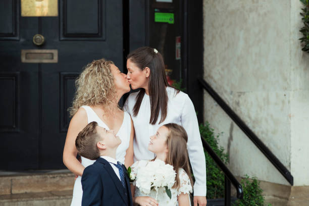 Wedding Day Kiss A front-view shot of a happy newlywed lgbtqi couple kissing each other, they are standing with their proud family on their wedding day. gay wedding kiss stock pictures, royalty-free photos & images