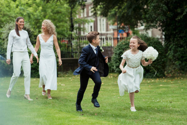 The Happiest Family! A front-view shot of a happy couple walking together on their wedding day, two young children can be seen being mischievous and running on the grass. ring bearer stock pictures, royalty-free photos & images