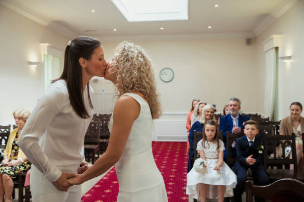 Remembering this Moment Forever! A side-view shot of two beautiful brides kissing and holding hands while saying their vows on their wedding day. gay wedding kiss stock pictures, royalty-free photos & images