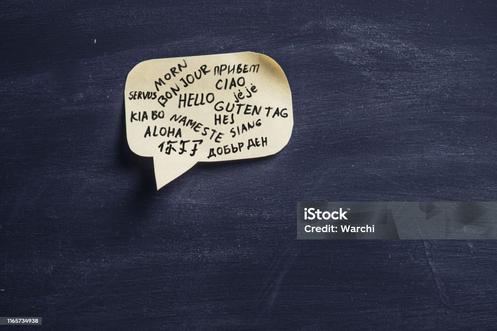 Hello in many languages. Adhesive note cut in form of a Speech bubble on blackboard  showing the word Hello in many languages. Translation Stock Photo