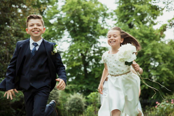 Carefree Wedding Fun A front-view shot of two young children being mischievous and running on the grass, they are having a fun time together. ring bearer stock pictures, royalty-free photos & images