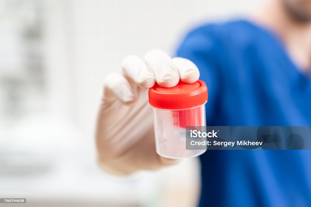 doctor in blue uniform and latex gloves is holding an empty plastic container for taking urine samples, light background. Medical concept. doctor in blue uniform and latex gloves is holding an empty plastic container for taking urine samples, light background Drug Test Stock Photo