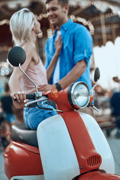 istock Red and white motorbike with two people next to it 1165744663